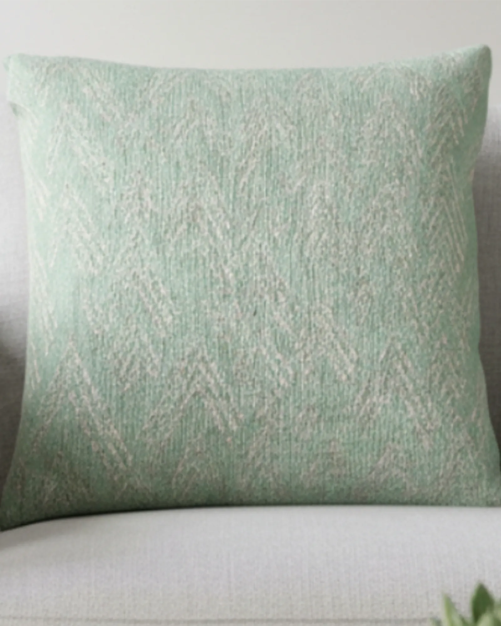 A preview of the Fresh Green Mint Ikat Woven Pillow showing a fresh green background and ivory white chevron ikat styled lines on a couch. 