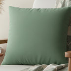 Green Dust faux suede pillow case styled on a wooden armchair in a modern living room.