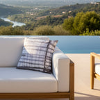 Grey watercolor plaid outdoor pillow styled on a villa terrace, overlooking a scenic landscape with a lake and hills,  patio lifestyle shot.