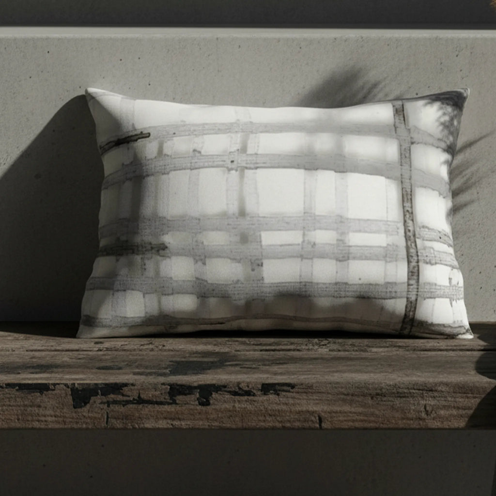 Grey watercolor plaid outdoor lumbar pillow on weathered wood bench, editorial lifestyle shot.
