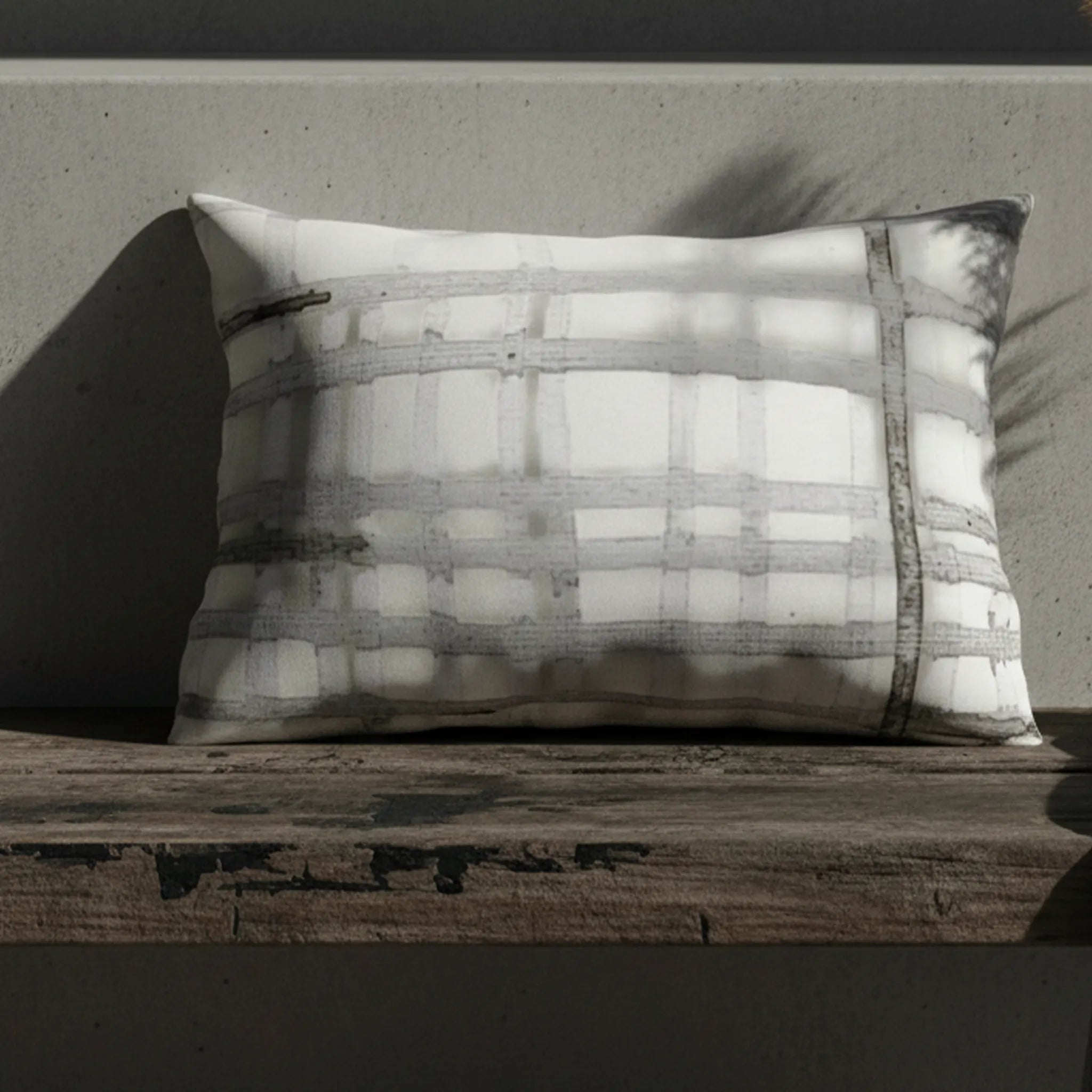 Grey watercolor plaid outdoor lumbar pillow on weathered wood bench, editorial lifestyle shot.