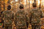 a group of three hunters shown from behind in a wooded fall setting wearing Realtree camo long sleeve tee with personalized back text.