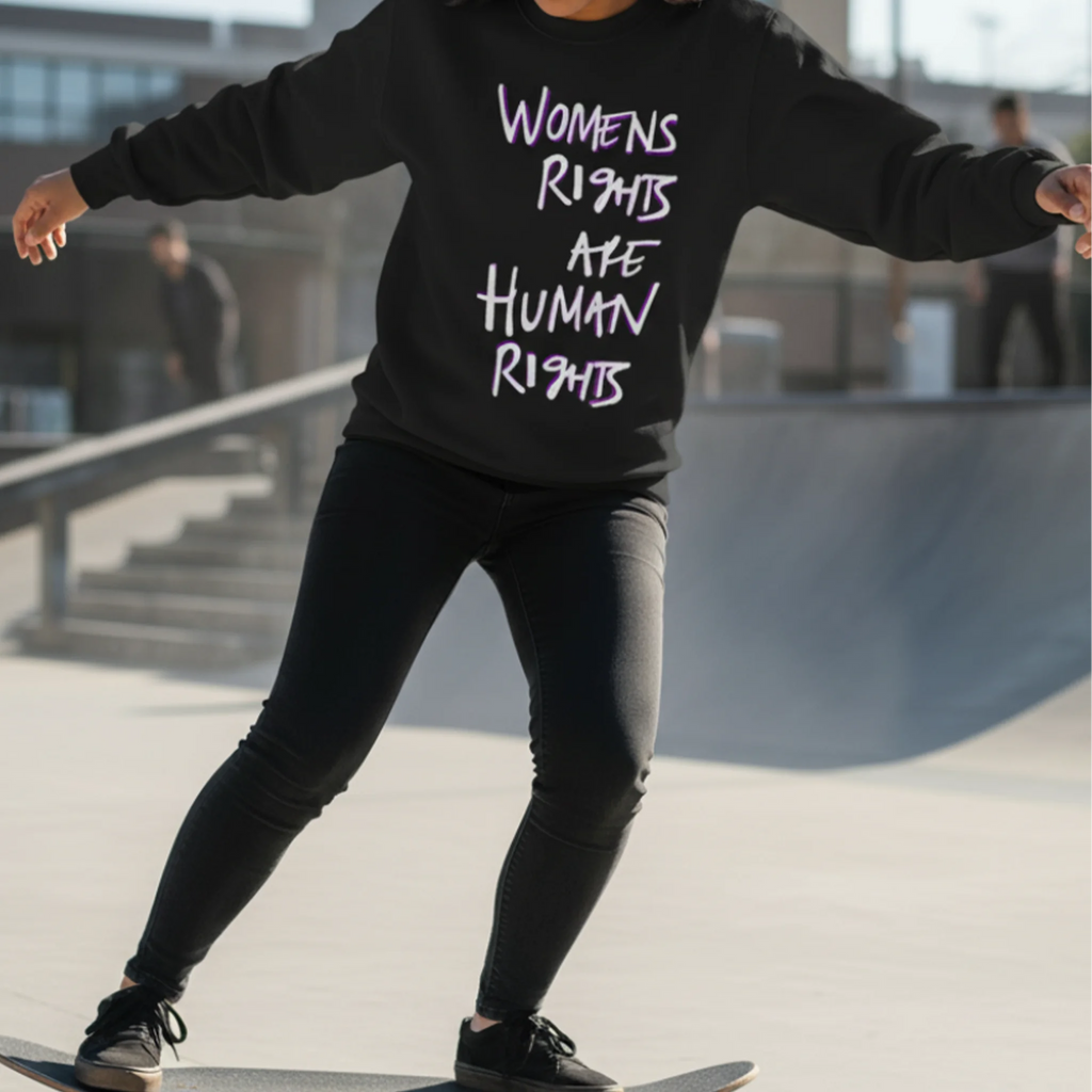 Jet Black Women's Rights sweatshirt, handwritten Womens Rights Are Human Rights graphic, crew neck, styled with black jeans at a skate park, action lifestyle front view.