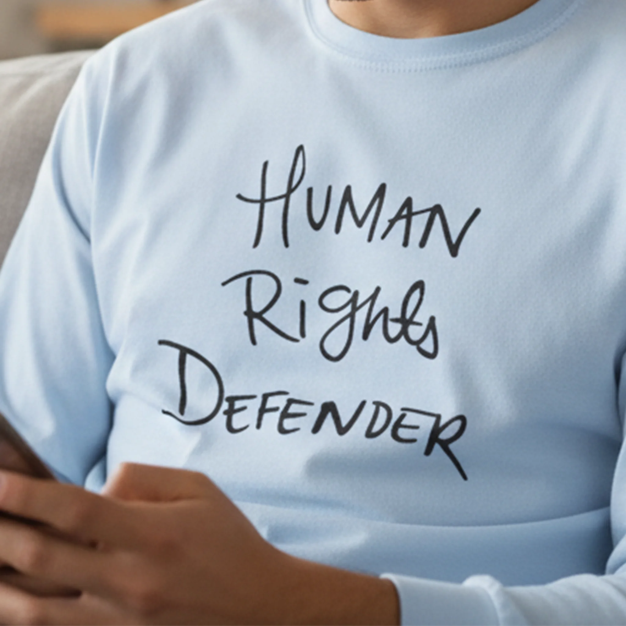 Light blue Human Rights Defender long sleeve tee, black graphic, cozy indoor lifestyle front view.