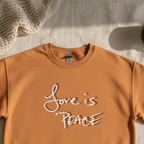 Burnt orange crewneck with Love is Peace lettering laid flat, overhead view.