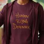 Maroon Human Rights Defender long sleeve tee styled with zip hoodie, retro ochre graphic, front view.
