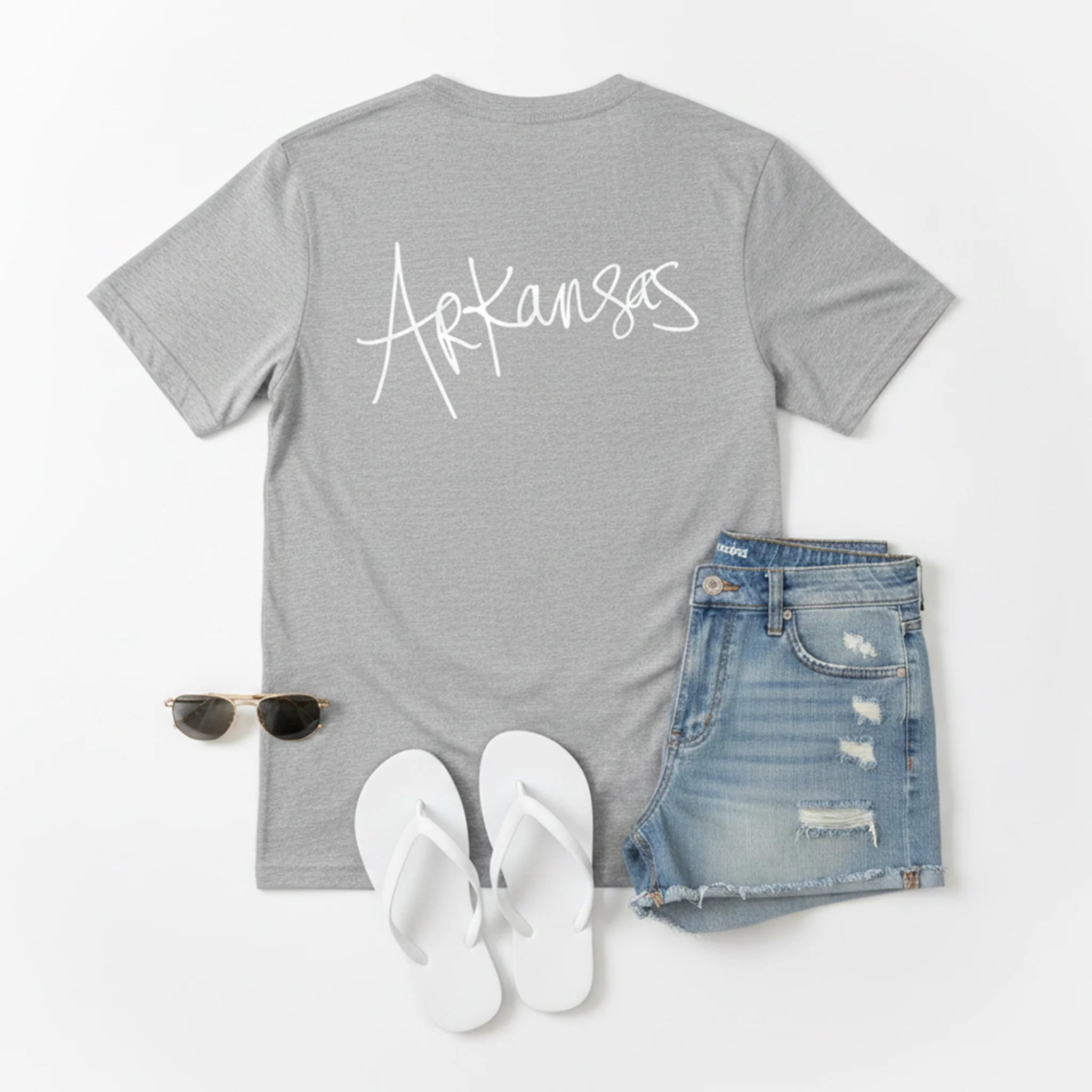 A back view of the Athletic heather, "Natural." Arkansas tee flat lay, ripped denim shorts, white flip flops, sunglasses, birds-eye view.