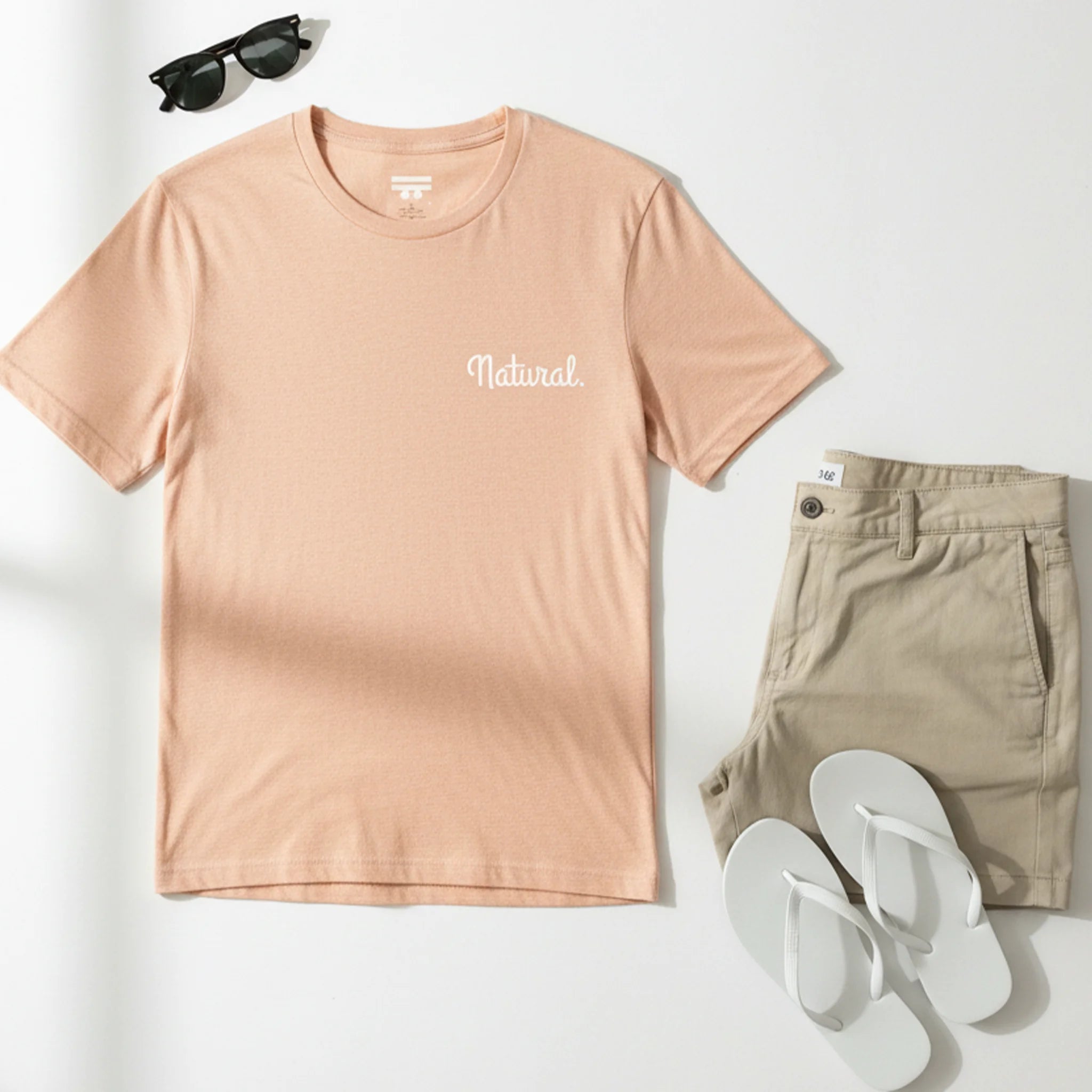 Heather peach Natural tee flat lay, khaki shorts, white flip flops, sunglasses, birds-eye view.
