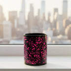 Freebrd Medicolo neon pink abstract black ceramic mug sitting on a windowsill with soft golden sunrise light and blurred urban city skyline in the background.