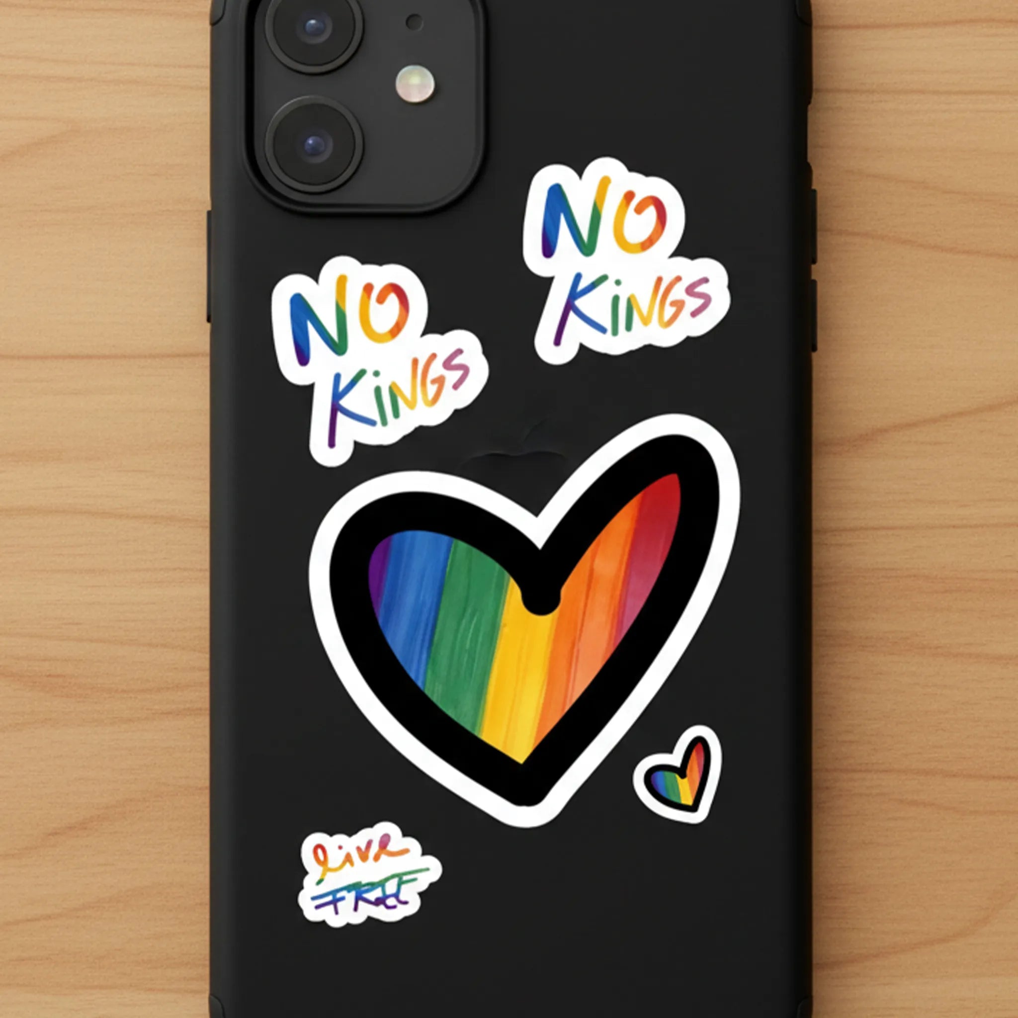 No Kings Pride Rainbow Vinyl Decal Set, stickers on black phone case, warm wood surface, FREEBRD Pride Gear.
