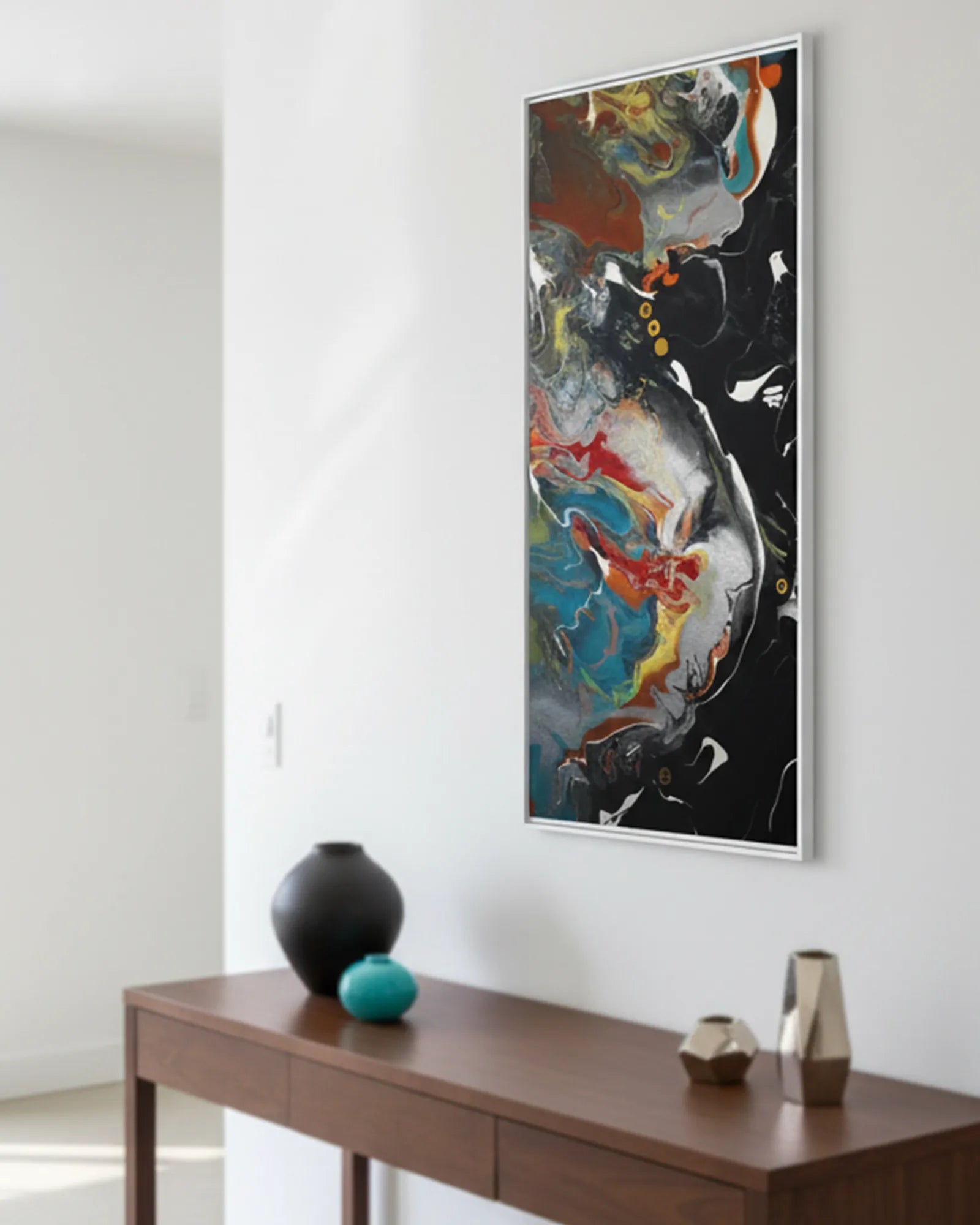 The white framed  ‘Silver Bird’ FREEBRD abstract painting on a white wall above a brown wooden console table with decorative decor items.