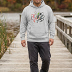 Man wearing a heather grey hoodie with a multicolored octopus chest graphic on a lakeside boardwalk with autumn foliage, front view.