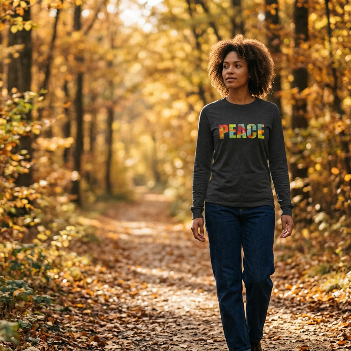 Woman wearing a dark-grey long-sleeve tee with multicolored PEACE lettering, standing on an autumn path.