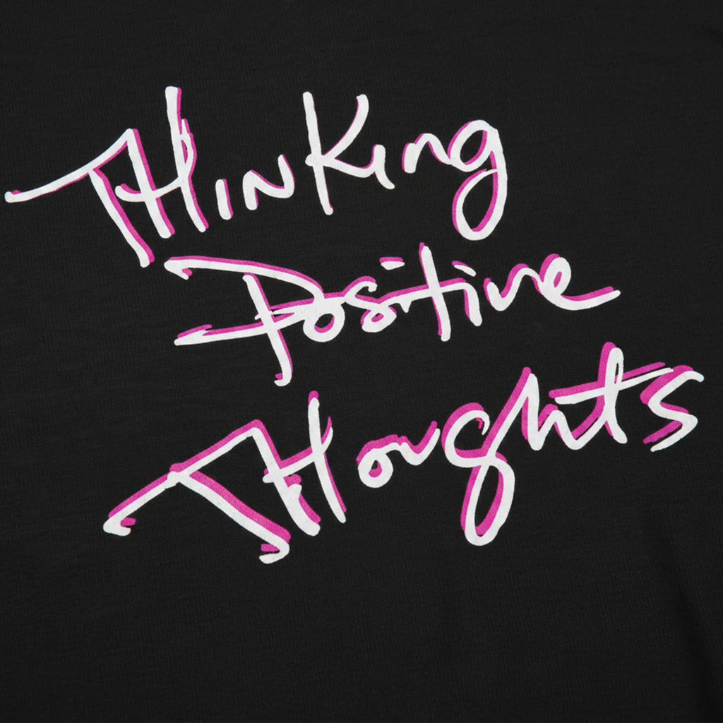 Classic fit crew neck tee, black, close-up texture showing cotton fabric weave and handwritten script graphic reading Thinking Positive Thoughts in white with hot pink outline.