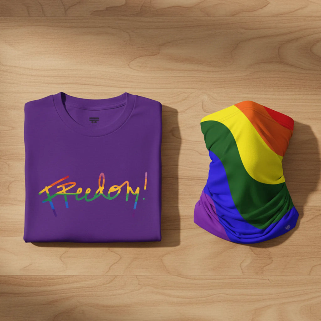 Purple t-shirt bundle with 'Freedom!' in rainbow colors and a rainbow flag on a wooden surface.