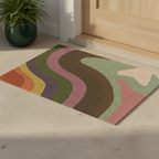 Multicolored pride doormat with wavy pattern on a beige floor next to a wooden door.