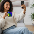 Woman on couch taking selfie with black FREEBRD rainbow wave ceramic mug showing purple blue and forest green.