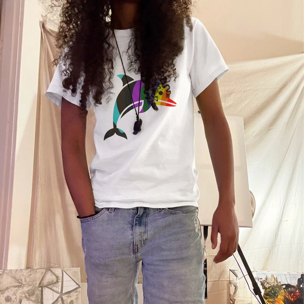 Person with long curly hair wearing a sand hoodie with a rainbow mountain and pine-tree chest graphic, a front pouch pocket, and olive pants in sunlight. 