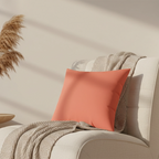 Salmon red faux suede pillow styled on a sofa chair, warm coral pink home decor.