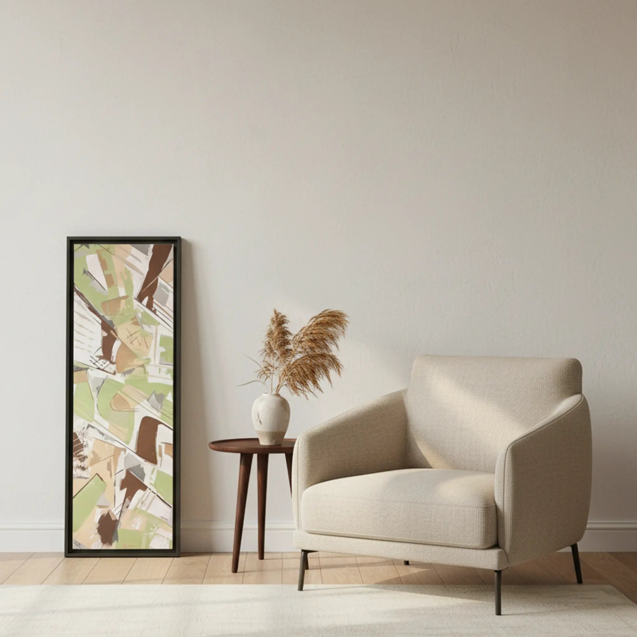 Freebrd "Slim Sage" framed abstract canvas art, 12x36 vertical, 1.25" thick, fully framed in black wood, leaning against modern interior wall beside accent sofa chair — size reference in sage green, taupe, and muted brown.