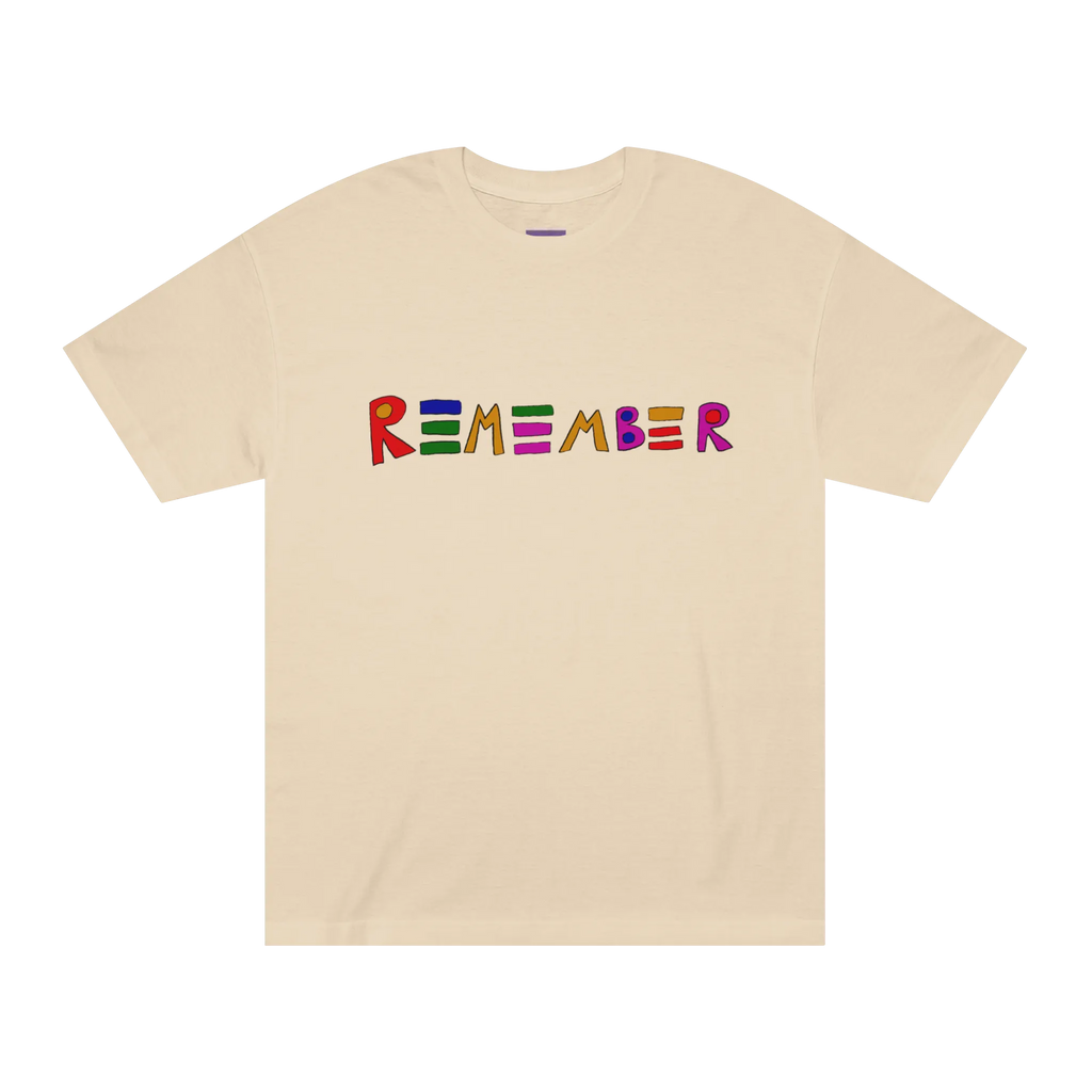 Classic fit crew neck tee, sand, front view, hand-drawn multicolor lettering reading REMEMBER in red, blue, green, orange, purple, and pink.