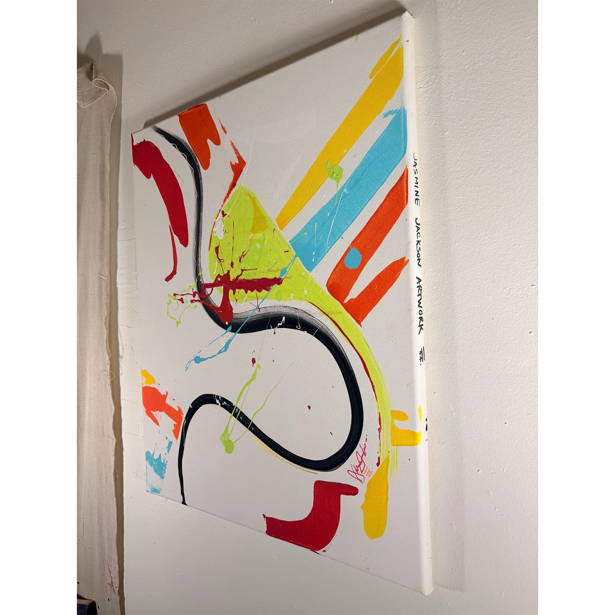 Angled view of an abstract acrylic painting showing the canvas depth, handwritten FREEBRD artist name Jasmine Jackson Artwork along the edge, and colorful marks across a white ground.