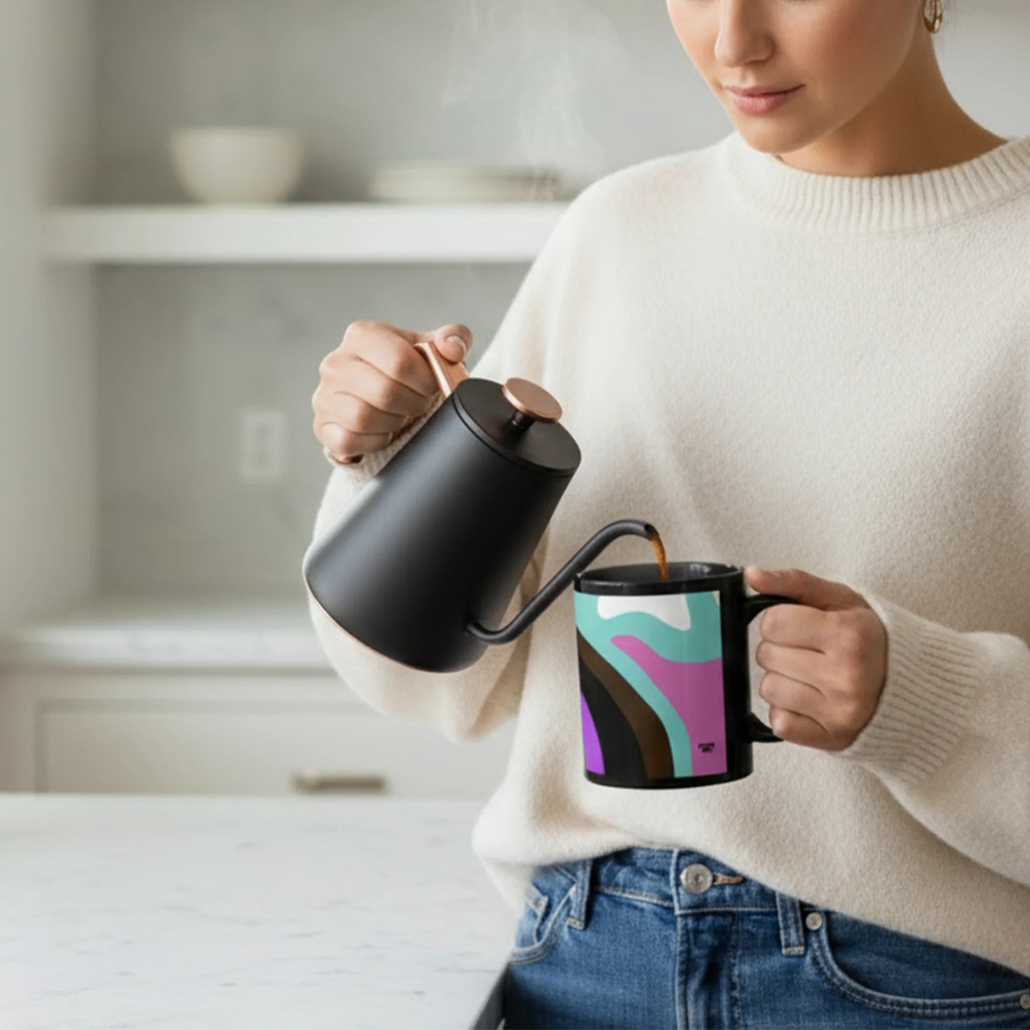A person pouring coffee from a gooseneck kettle into the Support Love Ceramic Mug, showing the abstract pride wave design on the glossy black 11oz cup in a modern kitchen