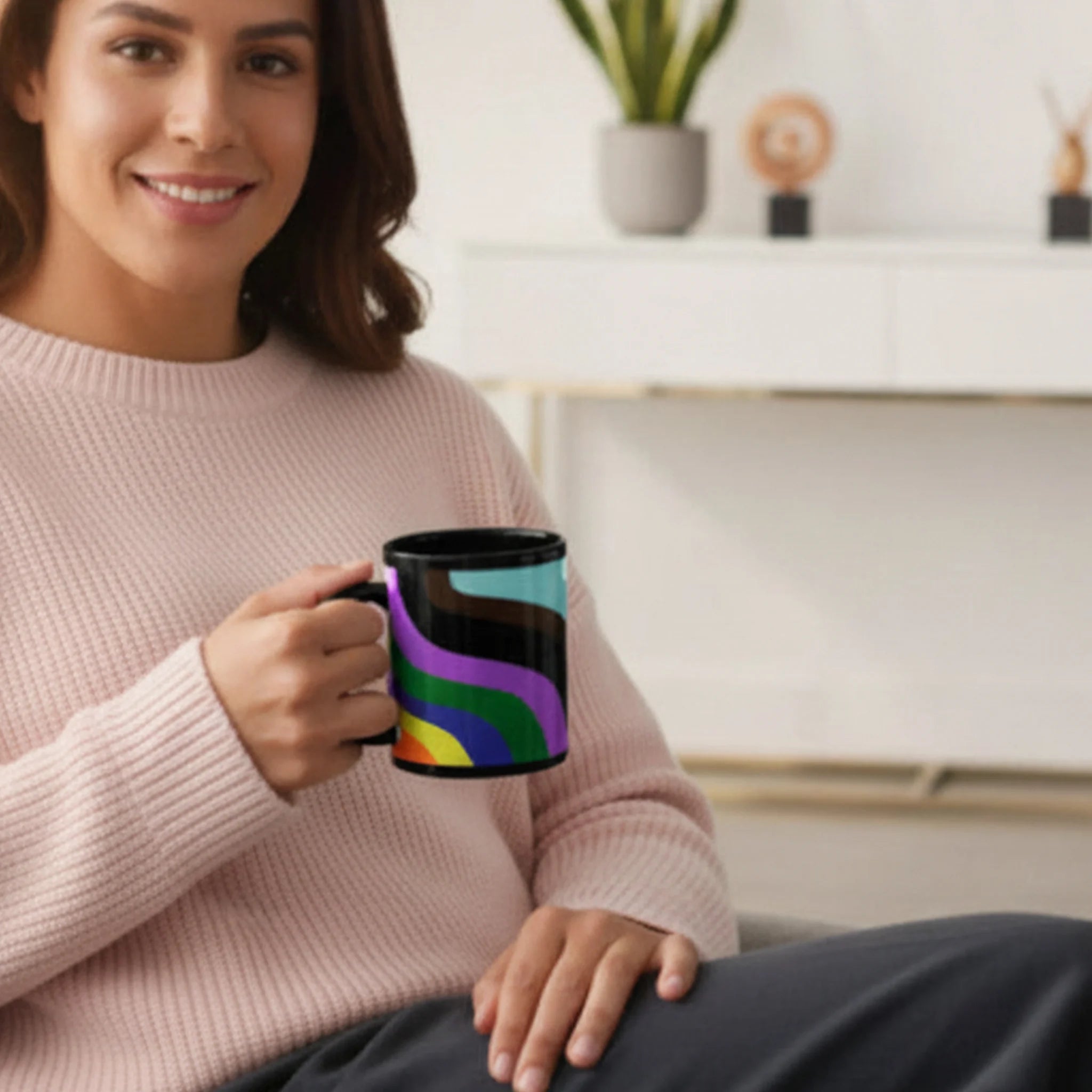 A smiling person holding the Support Love Ceramic Mug featuring a colorful abstract pride wave design on a glossy black 11oz ceramic mug in a cozy living room setting.