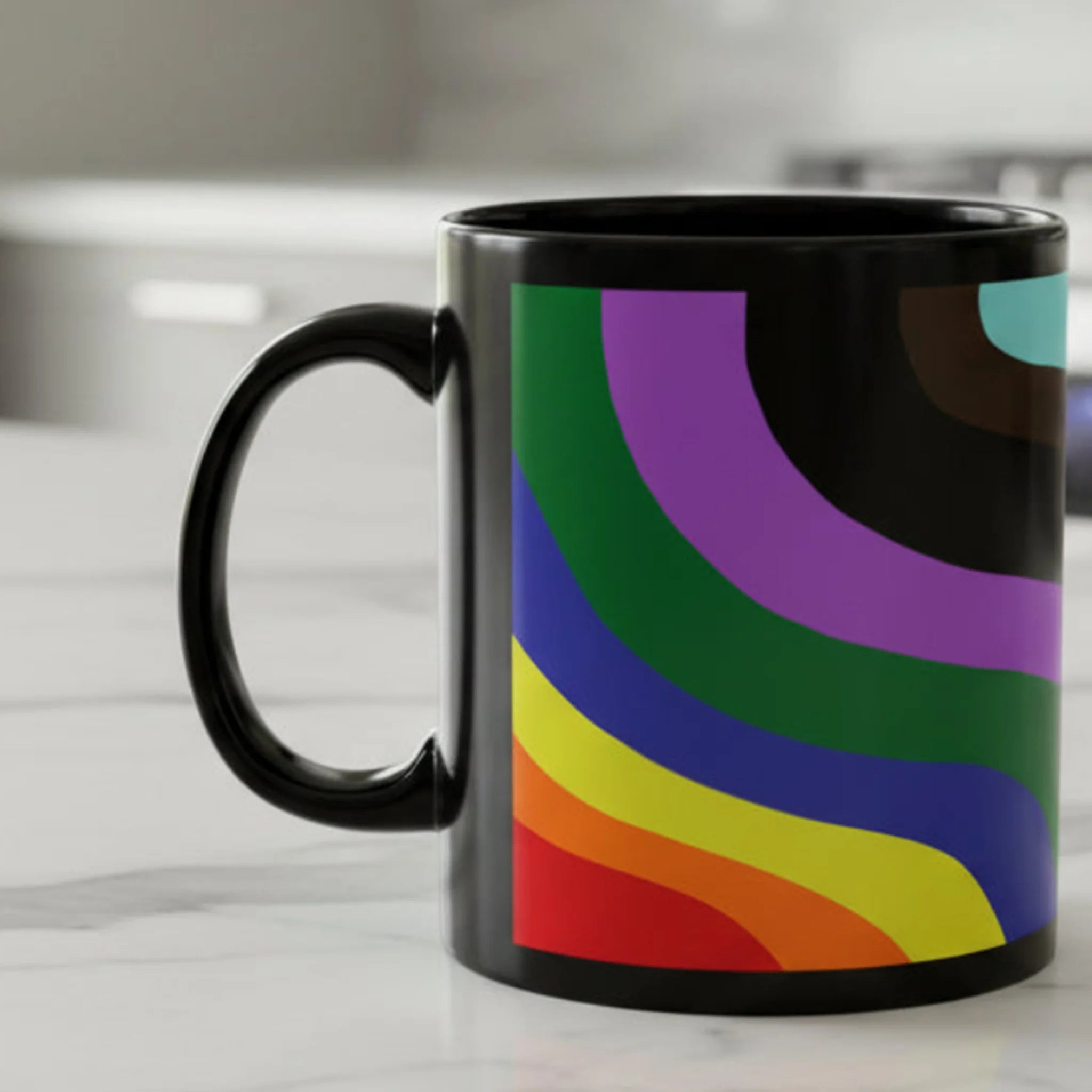 A right side view of the Support Love Ceramic Mug displaying bold rainbow wave stripes in red, orange, yellow, green, blue, and purple on a glossy black 11oz ceramic mug on a white kitchen counter.