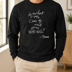Person wearing a black long-sleeve top with white handwritten quote artwork and light khaki pants, standing in a softly lit room.