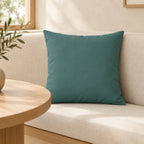 Teal Grey square pillow cover on an ivory upholstered banquette beside a pale wood table.