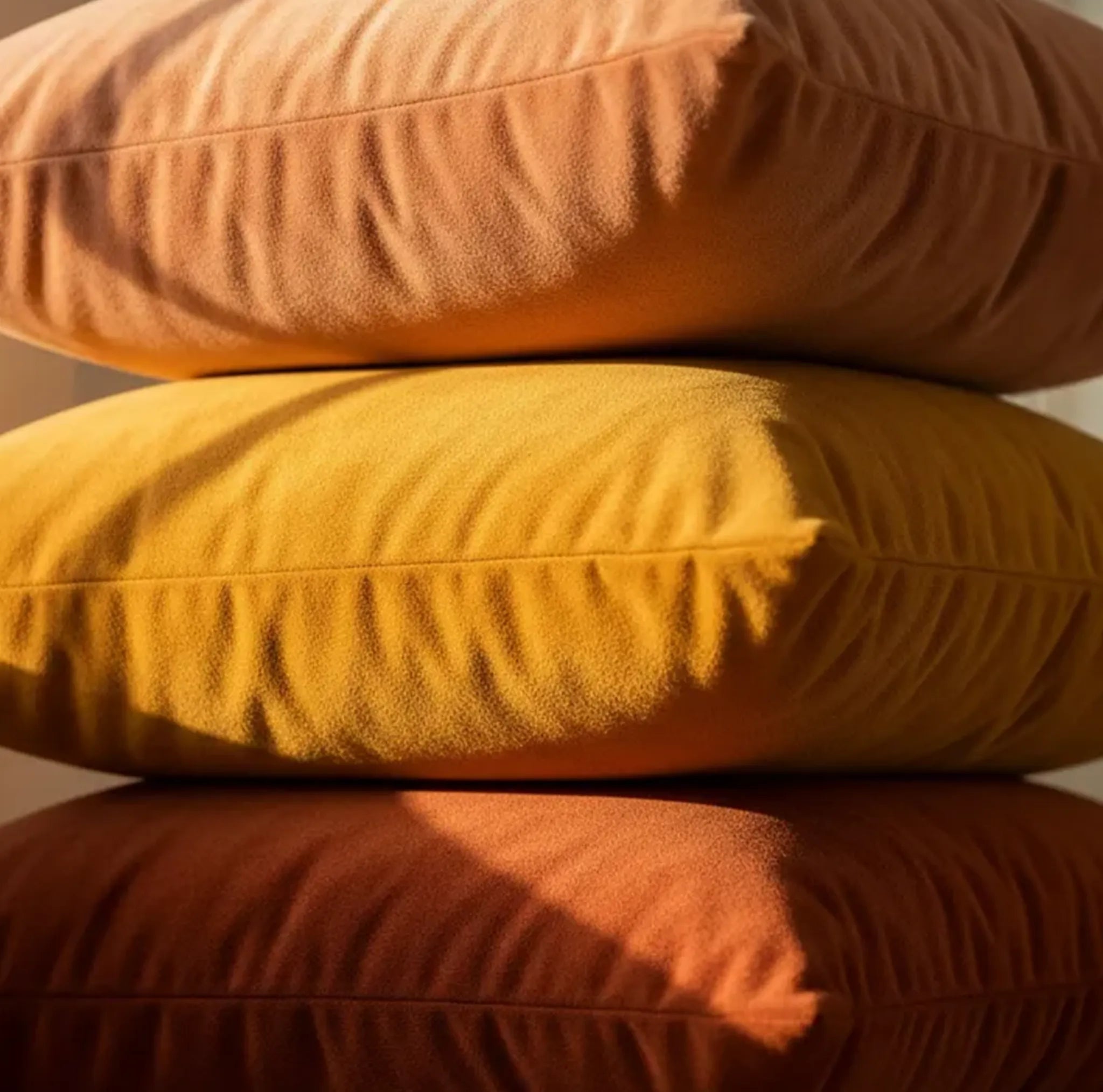 Stack of three hues of earth and solstice terracotta orange pillows with a warm glow.