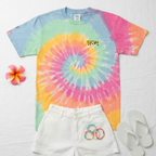 A bird's eye flat lay of the pastel sherbet tie-dye cheetah embroidered tee styled in a unisex summer outfit with white linen shorts, colorful beaded bracelets, white flip flops, and a tropical flower on a white linen surface.