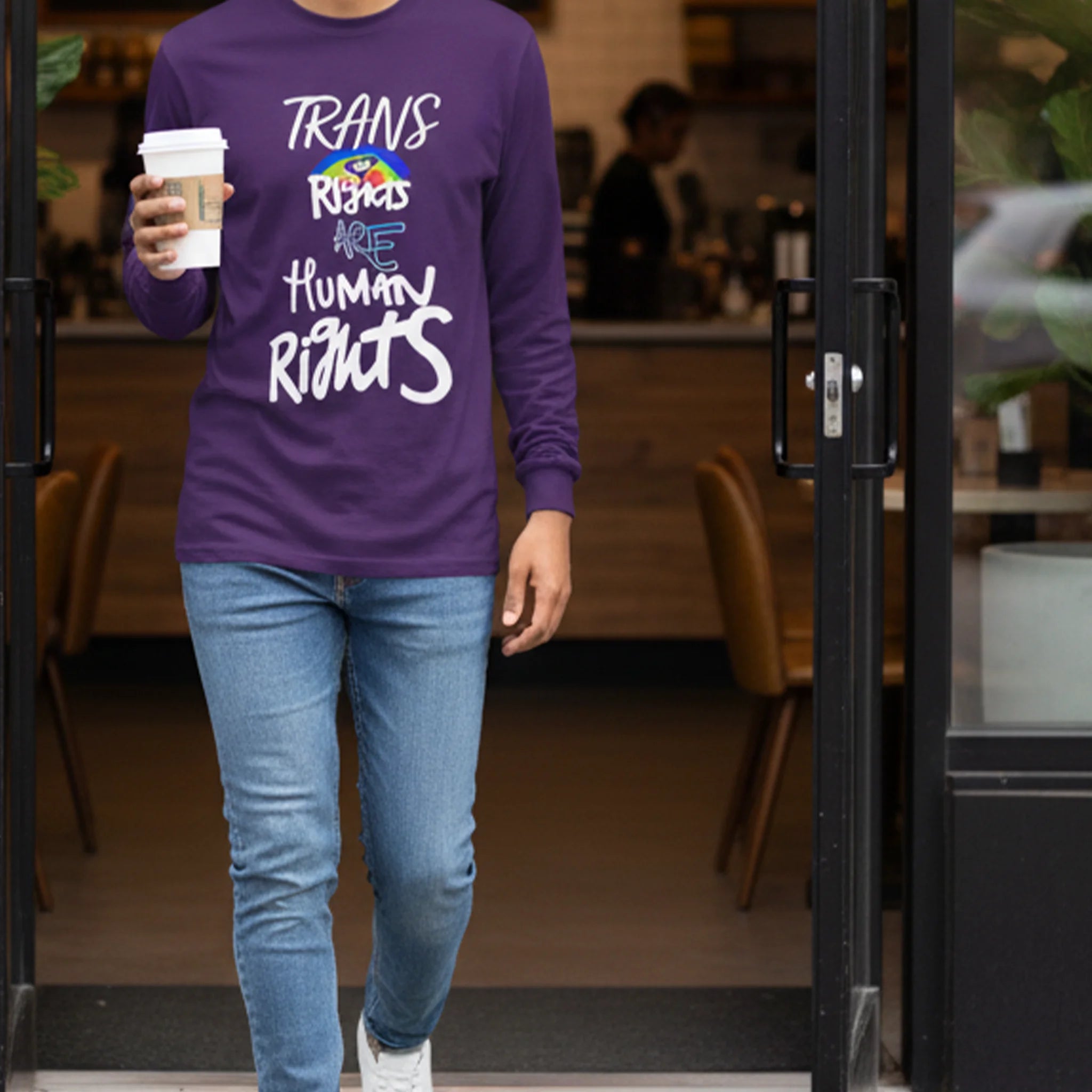 Person wearing a Freebrd designed purple shirt with a positive message, holding a coffee cup, walking through a doorway.
