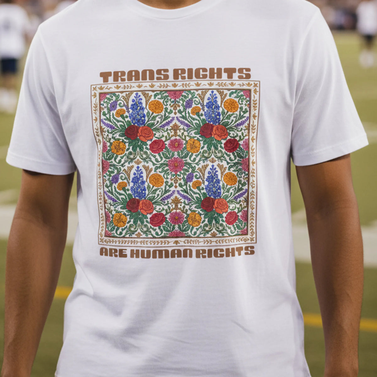 White Trans Rights Are Human Rights floral graphic tee worn by a man at an evening American football game, front view.