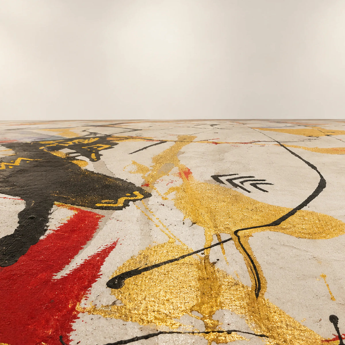 Painted floor with gold and red patches, flowing black lines, and zigzag marks on white, receding toward a plain off-white wall.