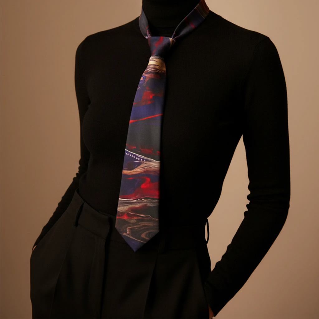 Tribal Wave wearable art necktie worn by woman, abstract navy, red and charcoal print, black turtleneck, sleek editorial lifestyle.