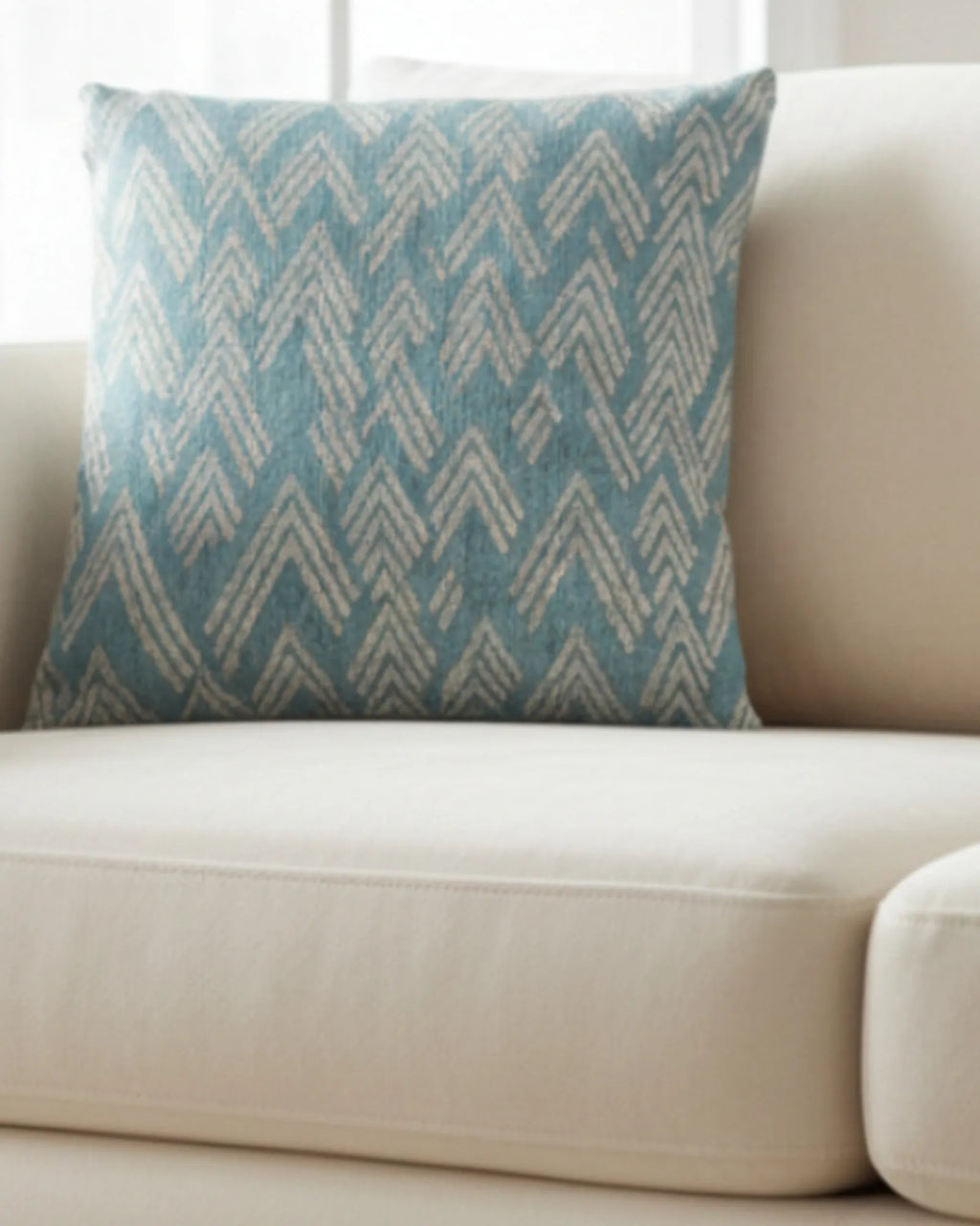 A lifestyle view of the Vintage Aqua Ikat Patterned Woven Throw Pillow showing a vintage aqua background and ivory white chevron styled lines on a beige couch. 
