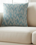 A lifestyle view of the Vintage Aqua Ikat Patterned Woven Throw Pillow showing a vintage aqua background and ivory white chevron styled lines on a beige couch. 