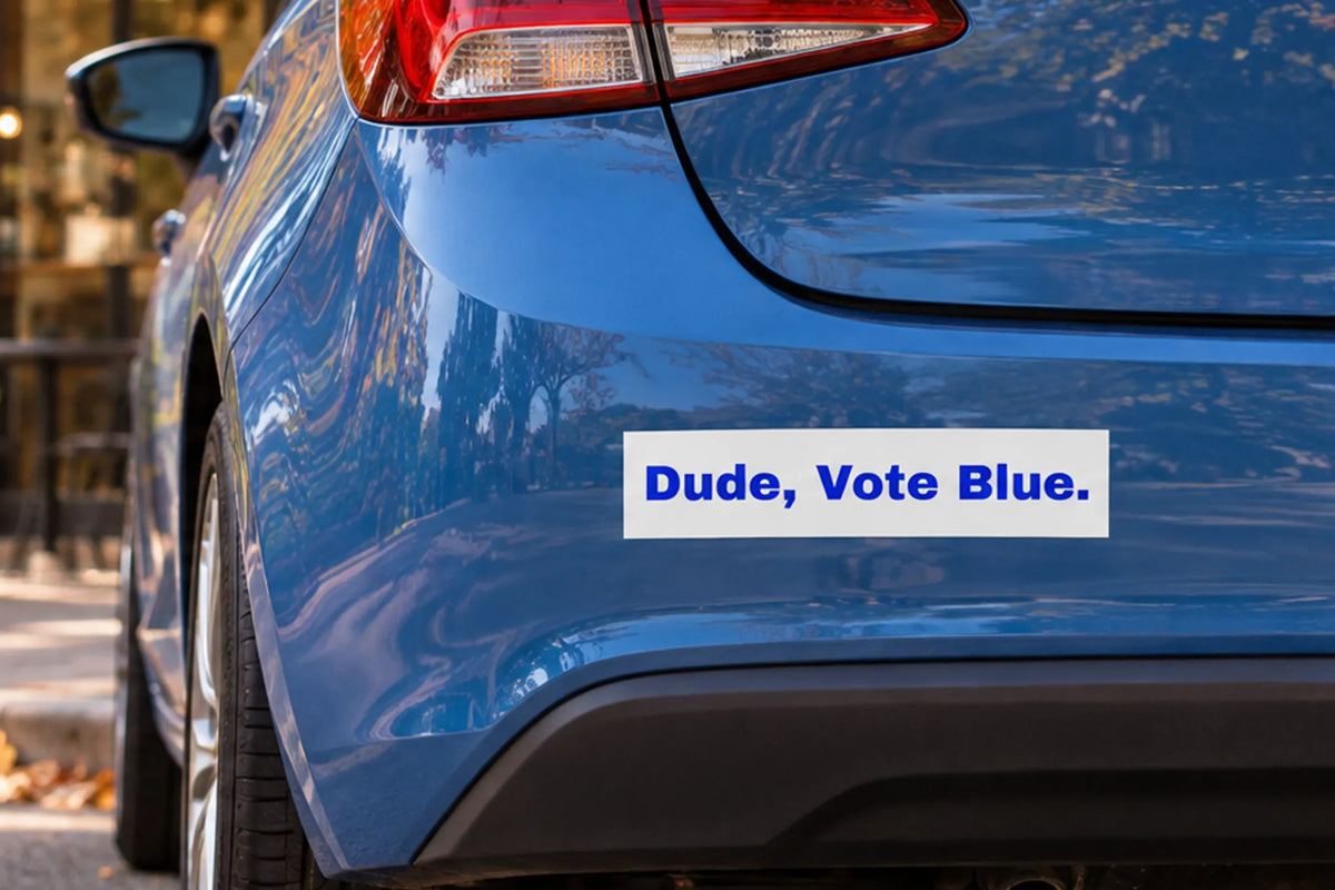 White sticker with blue 'Dude, Vote Blue.' lettering on the rear bumper of a blue hatchback parked outside a coffee shop.