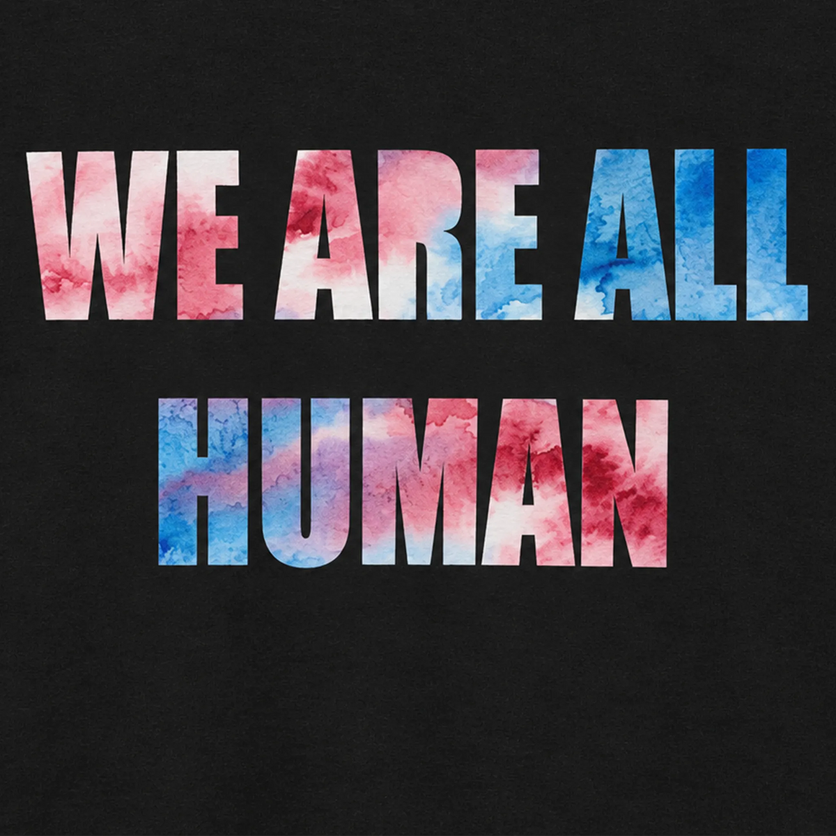 Close-up of a black T-shirt showing ‘WE ARE ALL HUMAN’ in pink, white, and blue watercolor-style lettering across the chest.