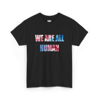 Black crew neck T-shirt with ‘WE ARE ALL HUMAN’ across the chest in pink and blue watercolor-style lettering, front view.