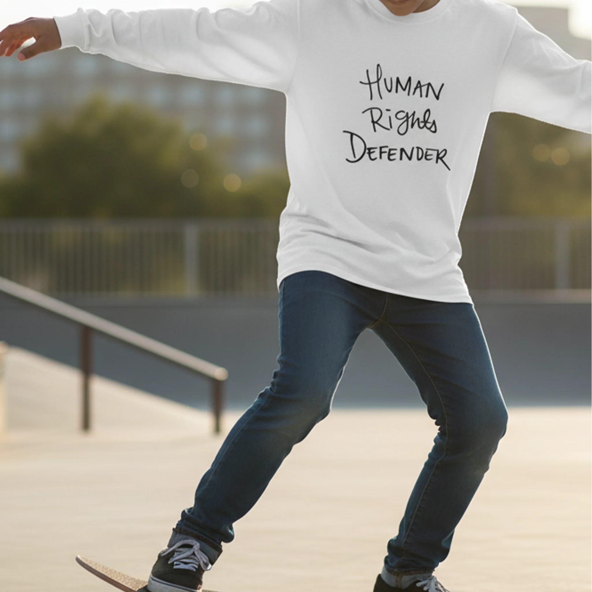 White Human Rights Defender long sleeve tee, black graphic, skate park lifestyle front view.