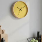 The champ yellow silent wall clock, wooden base, black hands, light grey markers, styled on a kitchen wall, 10 inch, front view.