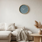 Danish blue wall clock with wooden base and white hands styled in minimalist Scandinavian living room with a beige sofa, blanket and a decorative plant.