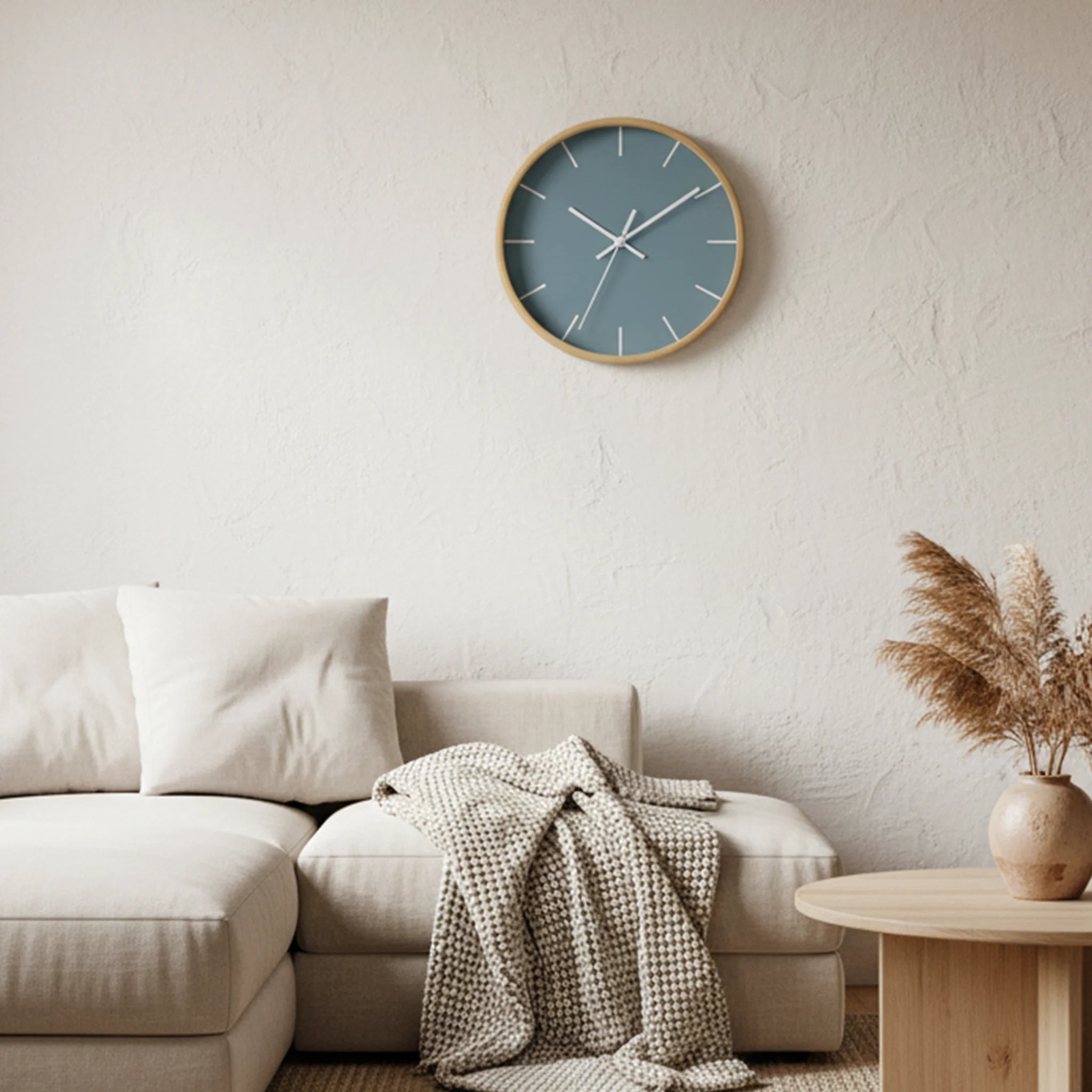Danish blue wall clock with wooden base and white hands styled in minimalist Scandinavian living room with a beige sofa, blanket and a decorative plant.