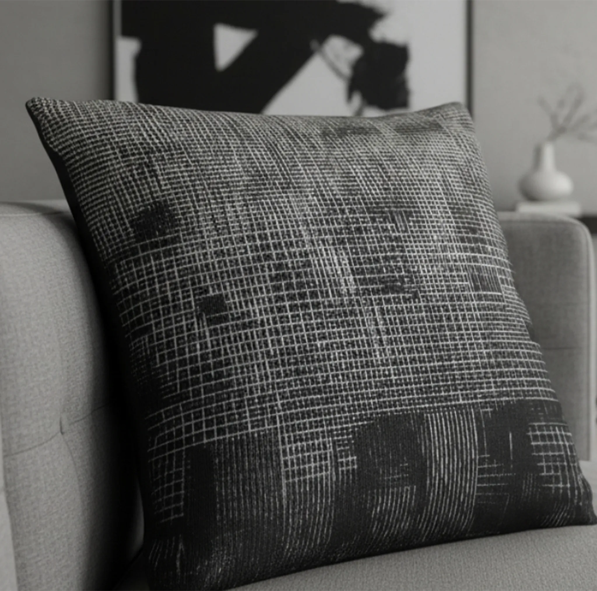 The textured ‘Geometric Net' pillow on a sofa with a blurred abstract painting in the background